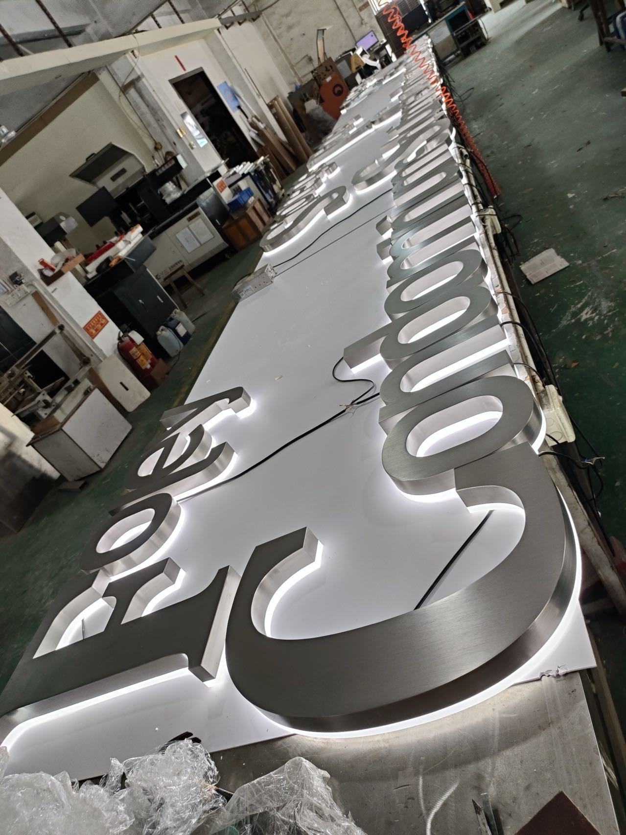 Large brushed stainless steel halo-lit letters undergoing illumination testing in a signage workshop